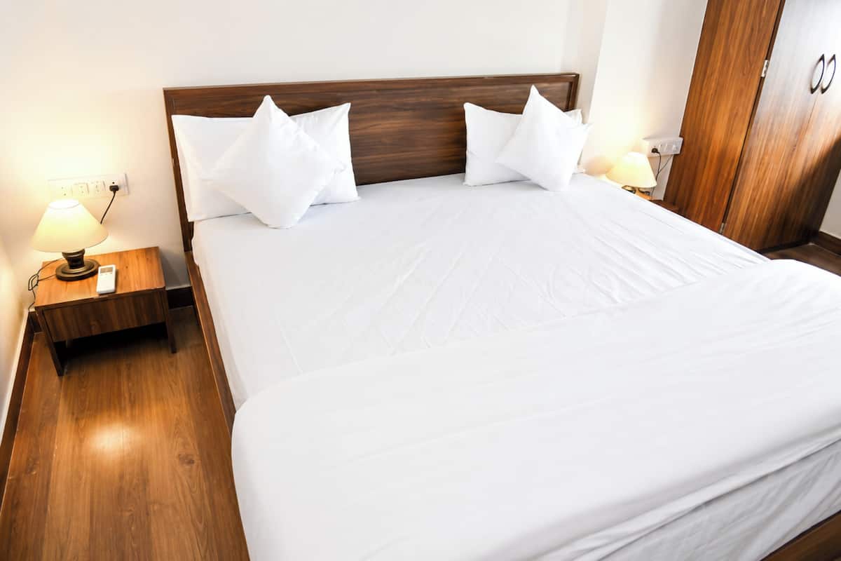 Una cama bien tendida con sábanas y almohadas blancas, cabecera de madera y lámparas de noche.