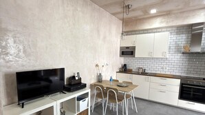 Una cocina moderna con armarios blancos, una mesa de comedor con sillas, un televisor empotrado y un microondas.