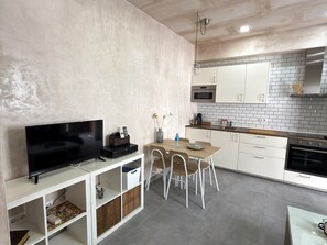 Une cuisine moderne avec des meubles blancs, une table à manger avec des chaises, un téléviseur encastré et un four à micro-ondes.