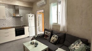 Un espacio habitable compacto con kitchenette, un sofá con cojines estampados y una mesa de centro de vidrio.