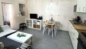 Un espacio habitable compacto con kitchenette, comedor, televisor sobre un mueble blanco y cama con almohada a rayas.