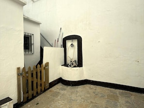 A narrow corridor with a wooden gate, a small window with bars, and a white wall with a black baseboard. - Novo home by Staycare (Rota)