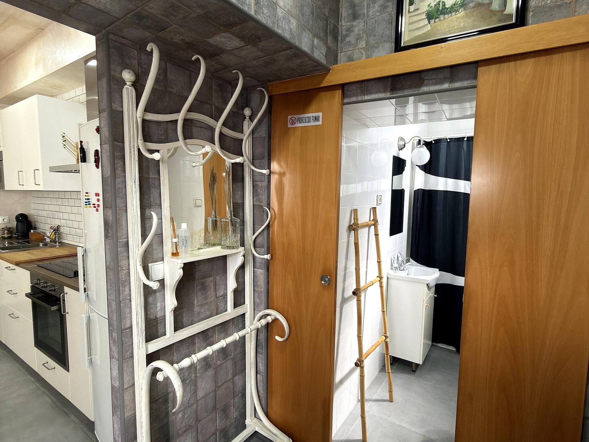 Une cuisine avec un réfrigérateur blanc, une cuisinière et un évier. On y trouve une porte en bois avec une pancarte au-dessus.