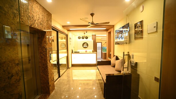 A hotel lobby with a reception desk, a ceiling fan, and a glass elevator. - ELORA'S INN (Siliguri)