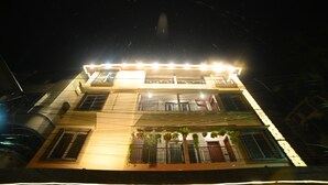 A multi-story building with balconies, outdoor plants, and a brightly lit facade at night. - ELORA'S INN (Siliguri)