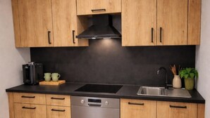 Een kleine keuken met houten kastjes, een vaatwasser, een zwart aanrecht en een klein spoelbakje.