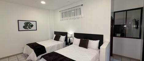 A hotel room with two beds, a nightstand with a lamp, a framed picture on the wall, and a window with curtains.