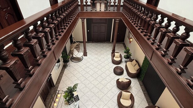 A spacious courtyard with a wooden balcony railing, multiple seating areas, and a central table with a keyboard and other items. - Hotel NASS del Sur (Cuenca)