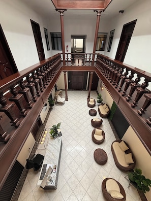 A spacious courtyard with a wooden balcony railing, multiple seating areas, and a central table with a keyboard and other items. - Hotel NASS del Sur (Cuenca)