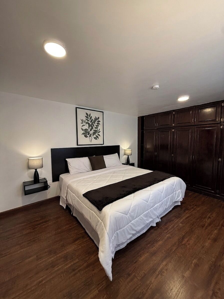 A neatly made bed with a headboard, bedside lamps, and a dark wooden wardrobe.