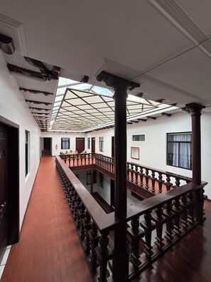 A corridor with a wooden railing, a tiled floor, and a skylight. - Hotel NASS del Sur (Cuenca)