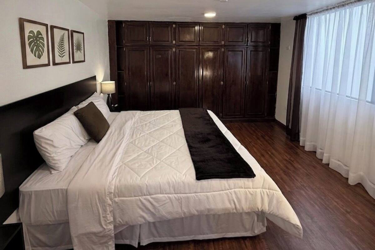 Une chambre avec un grand lit, une armoire en bois foncé et une fenêtre ornée de rideaux blancs.