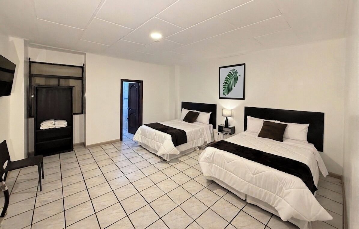 Habitación de hotel con dos camas, una silla, un televisor y una puerta que da a otra habitación.