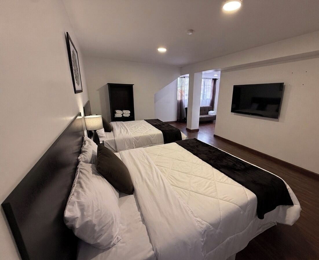 A hotel room with two beds, a flat-screen TV, a framed picture on the wall, and a staircase leading to another room.