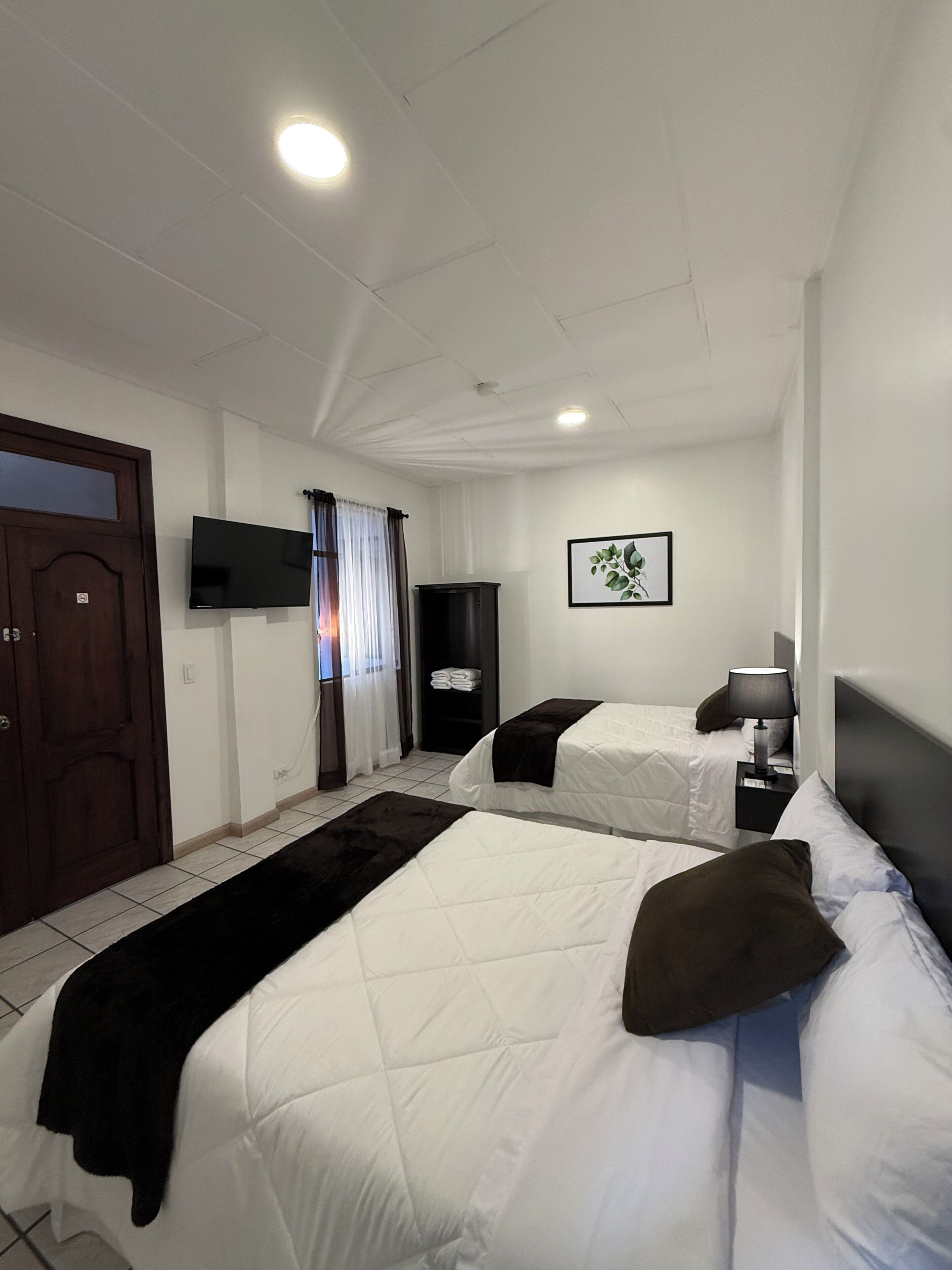 A hotel room with two beds, a flat-screen TV, a framed picture, and a door.
