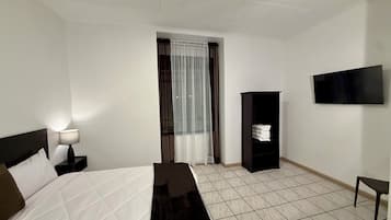 Una habitación de hotel con cama, mesita de noche, televisión, armario y ventana con cortinas.