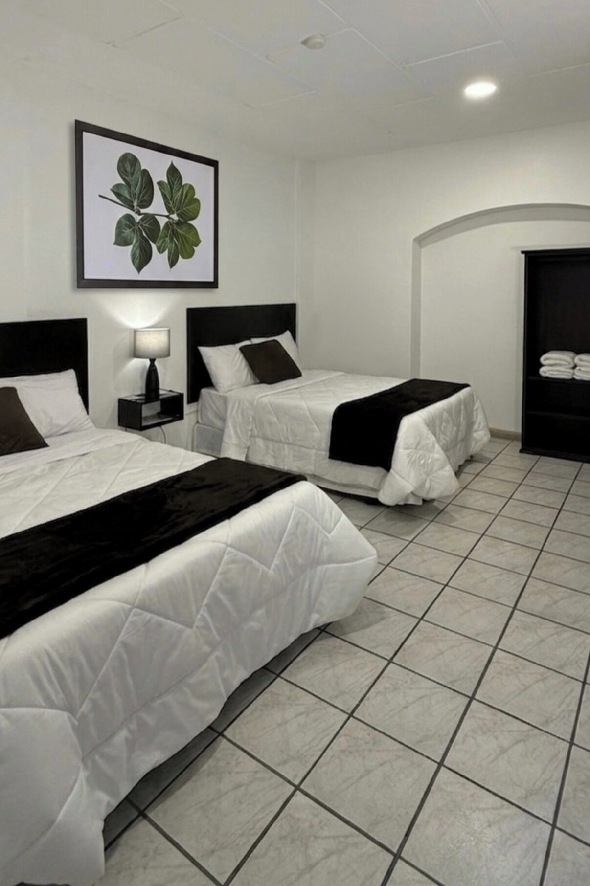 A hotel room with two beds, a framed plant, a nightstand, and a wardrobe.