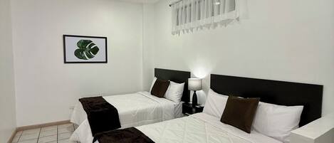 A hotel room with two beds, a ceiling fan, a window with sheer curtains, and a framed picture on the wall.