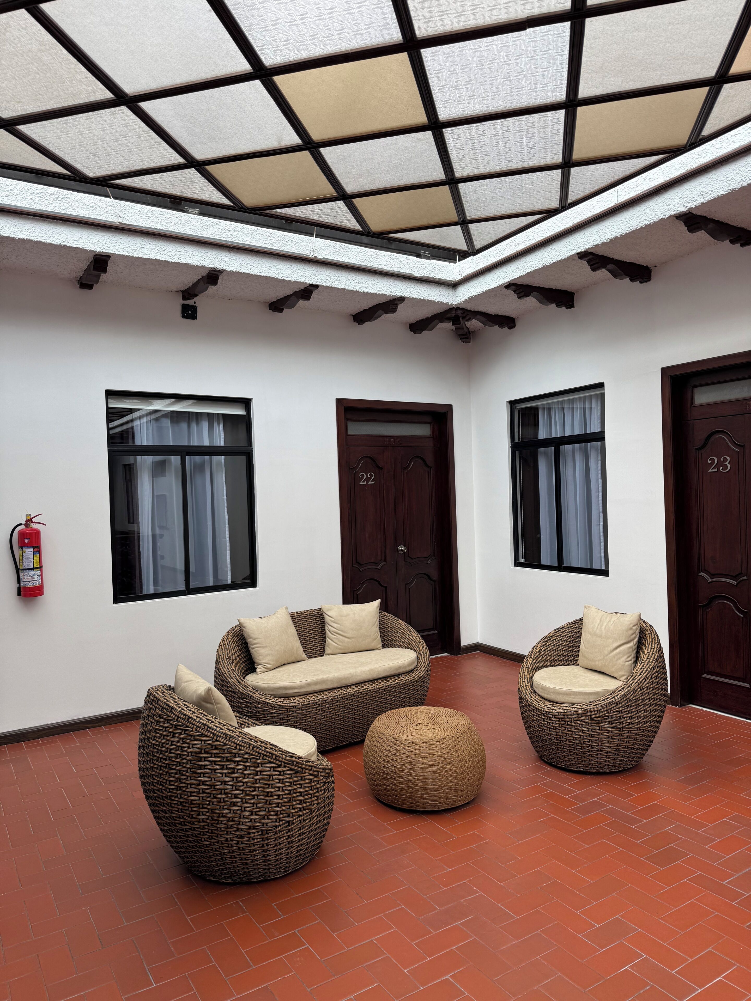Una habitación con techo alto, un extintor, un sofá, una silla y un pequeño reposapiés.