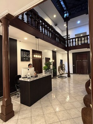 A hotel lobby with a reception desk, a computer, a plant, and a seating area. - Hotel NASS del Sur (Cuenca)