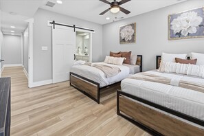 A bedroom with two beds, a ceiling fan, a large floral painting, and a sliding door leading to another room. - All New 3 Story House near Downtown Indy (Indianapolis)
