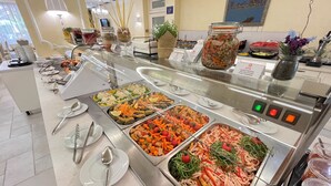 Noutopöytä, jossa on tarjolla monenlaista ruokaa, ruokailuvälineitä ja kyltti, joka ilmoittaa, että ruokaa saa ottaa niin paljon kuin haluaa.