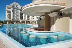 A large swimming pool with a curved edge, a multi-story building with balconies, and a clear blue sky. - Rena Alexandria Club hotel (Sunny beach)