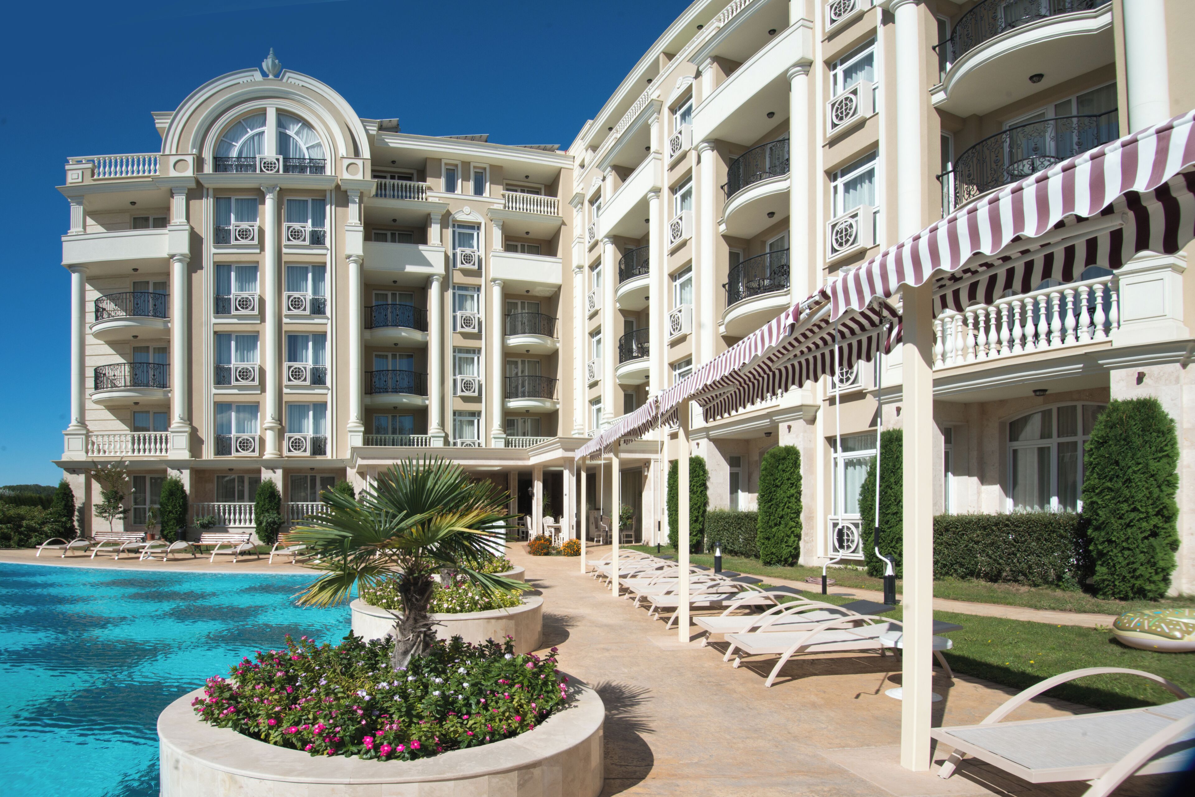 A large hotel with multiple balconies, a swimming pool, and sun loungers.