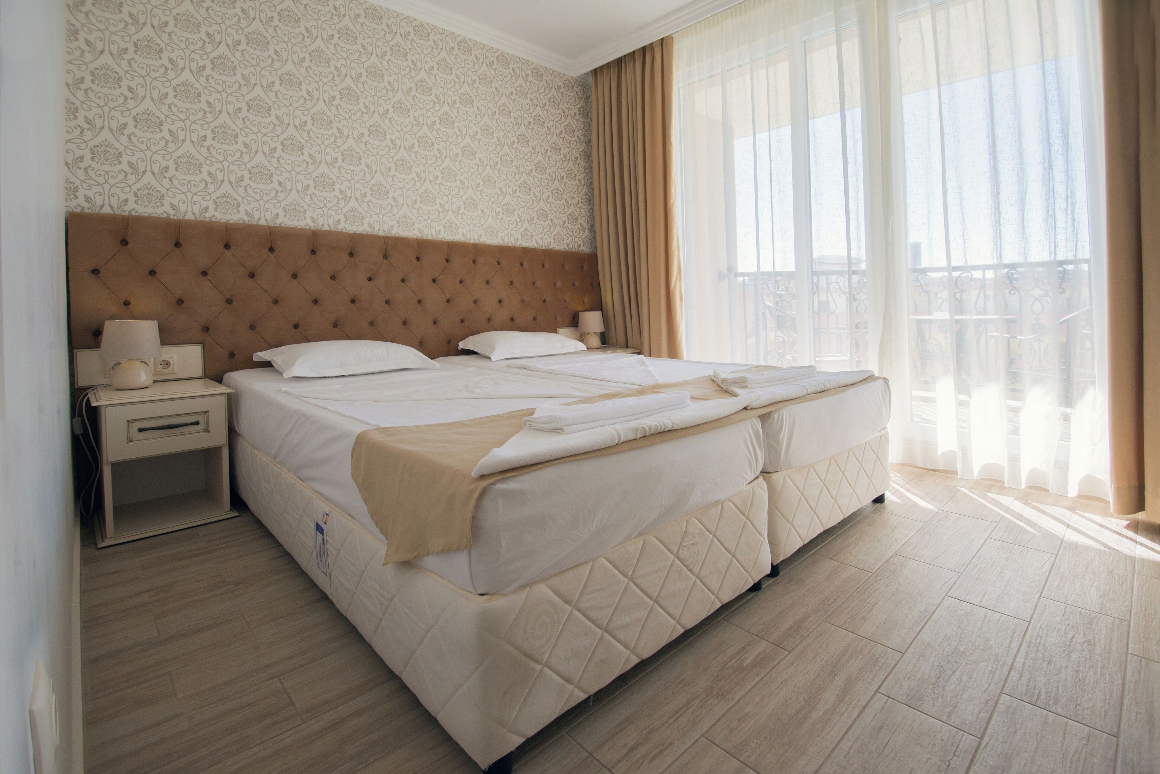 Une chambre d’hôtel avec un grand lit, une table de chevet, une lampe et une fenêtre avec des rideaux.
