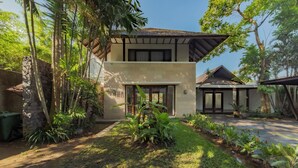 A two-story house with a stone wall, a covered porch, and a garden with tropical plants. - Villa SS Chang (Canggu)