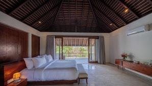A bedroom with a large bed, wooden headboard, bedside tables with lamps, a wooden bench, a nightstand, and a view through a glass door to an outdoor area. - Villa SS Chang (Canggu)