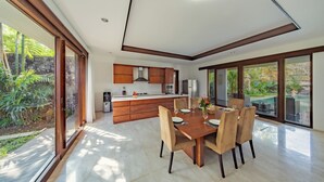 A modern kitchen with wooden cabinets, a central island, and a dining area with a table and chairs. - Villa SS Chang (Canggu)