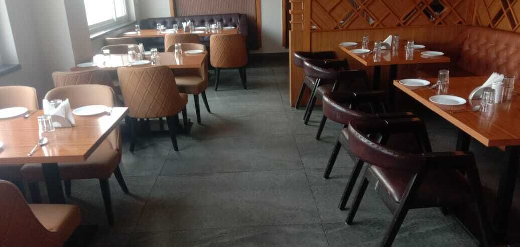 A restaurant with tables and chairs, a cushioned bench, and a tiled floor.