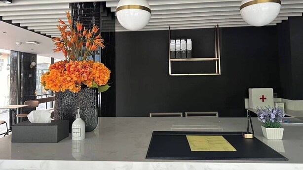 Un mostrador de recepción moderno con un jarrón de flores naranjas, un botiquín y un certificado enmarcado en la encimera.
