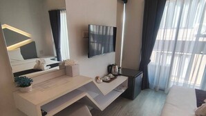 Una habitación de hotel moderna con una cama grande, un escritorio con televisor de pantalla plana, un espejo amplio y una ventana con cortinas.