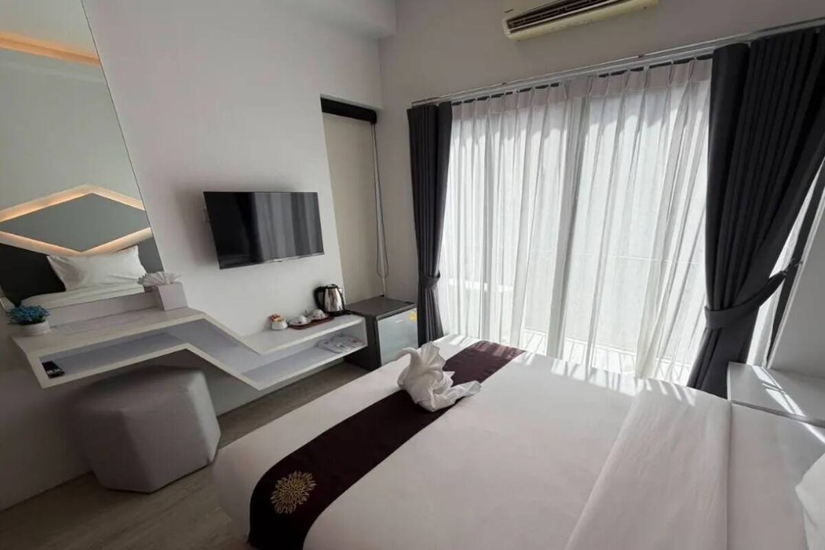 Una habitación de hotel moderna con cama, escritorio, televisor de pantalla plana y un ventanal con cortinas.
