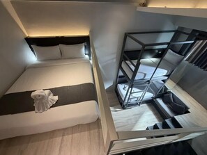 Una habitación de hotel compacta con cama, una pequeña zona de estar y una cama litera.
