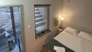 Makuuhuoneessa on sänky, yöpöytä, lamppu, taulu ja portaat, jotka johtavat ulkotilalle.