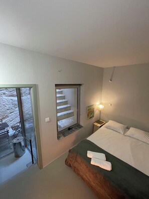 Ein Schlafzimmer mit Bett, Nachttisch, Lampe, einem Gemälde und einer Treppe, die zu einem Außenbereich führt.