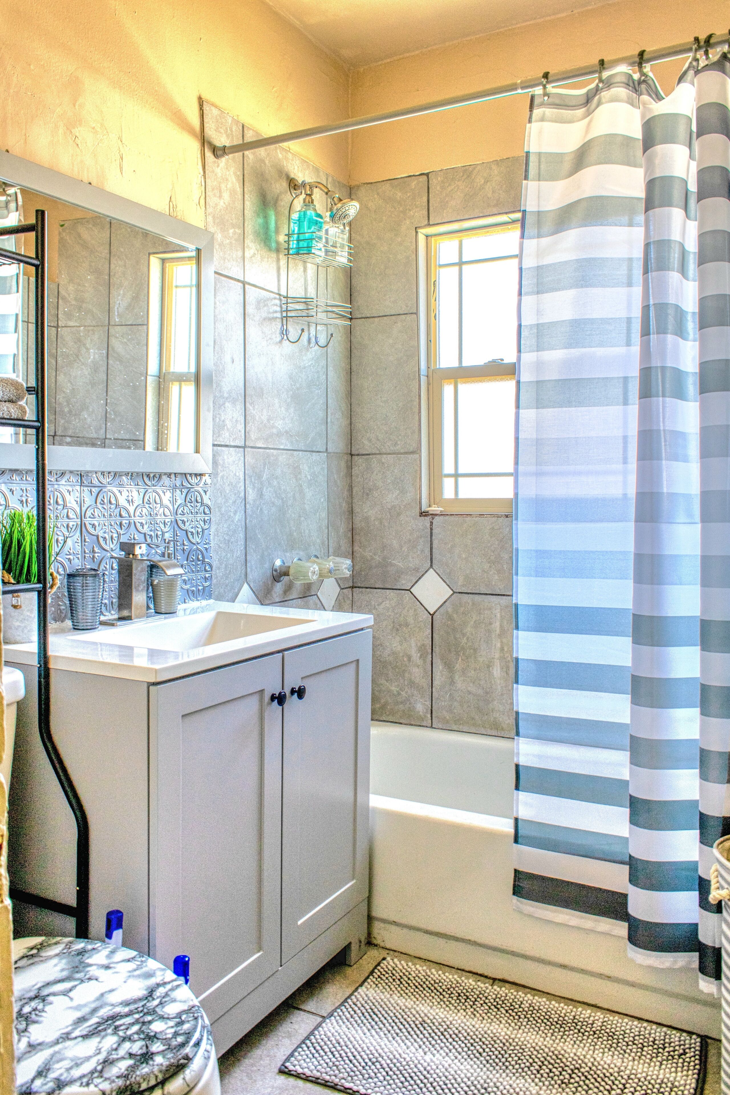 A bathroom with a bathtub, a shower curtain, a sink, a mirror, and a window.