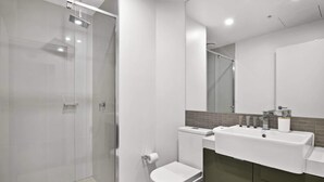 Un baño moderno con cabina de ducha de vidrio, inodoro blanco y lavamanos con espejo arriba.