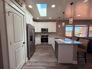 A modern kitchen with white cabinets, stainless steel appliances, a central island with seating, and pendant lighting.