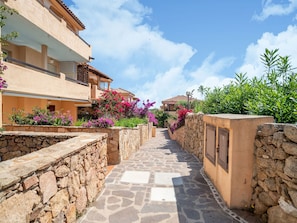 A narrow stone pathway flanked by buildings with balconies, leading to a building with a stone wall and a door. - Apartment in Sardinia Near Stunning Beaches (Golfo Aranci)