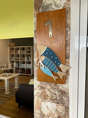 A wooden fish decoration with a number 1 on a wall, a bookshelf, a white table, and a stone wall. - Holiday Home in Porto da Cruz With Garden (Machico)