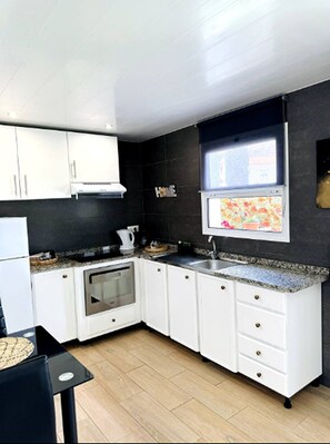 Uma cozinha moderna com armários brancos, forno embutido, pia de aço inoxidável e janela com vista colorida.