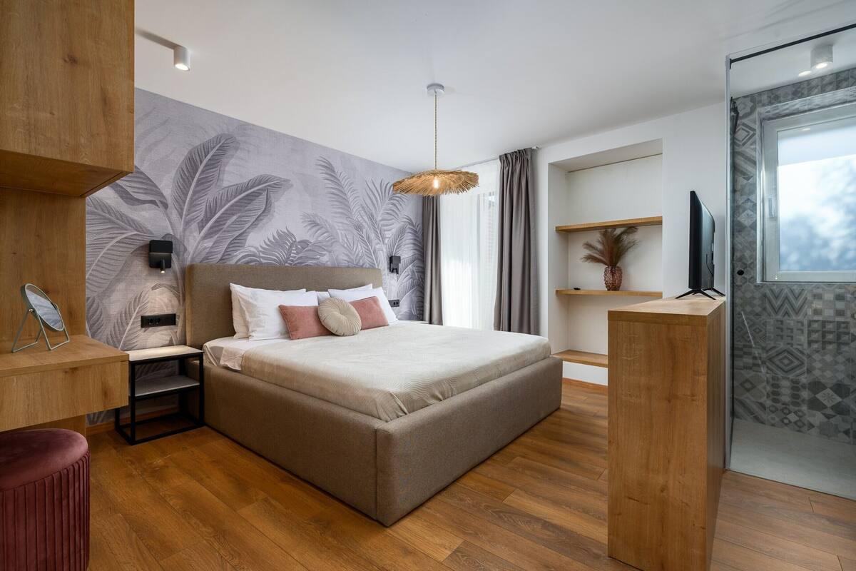 A modern bedroom with a large bed, a wooden desk, a TV, and a wall with a leaf pattern.