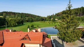 Un quartiere residenziale con una casa dal tetto rosso, uno stagno e una collina boscosa.