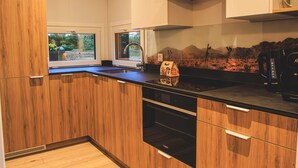 A modern kitchen with wooden cabinets, a black countertop, and a view of a garden through a window. - Modern Holiday Home With Infrared Sauna (Slagharen)
