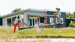 A modern house with a large deck, a wooden swing, and a metal swing set. - Modern Holiday Home With Infrared Sauna (Slagharen)