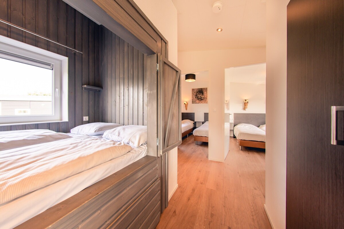 A modern bedroom with a wooden headboard, a large window, and a hallway leading to another room.